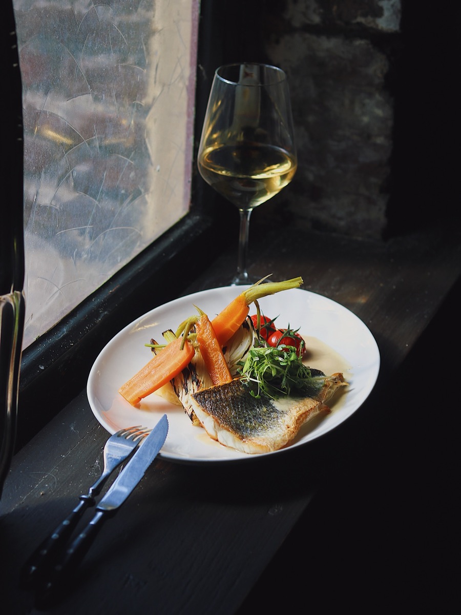 Dagverse vis met wortel en salade, geserveerd bij het raam met een glas witte wijn