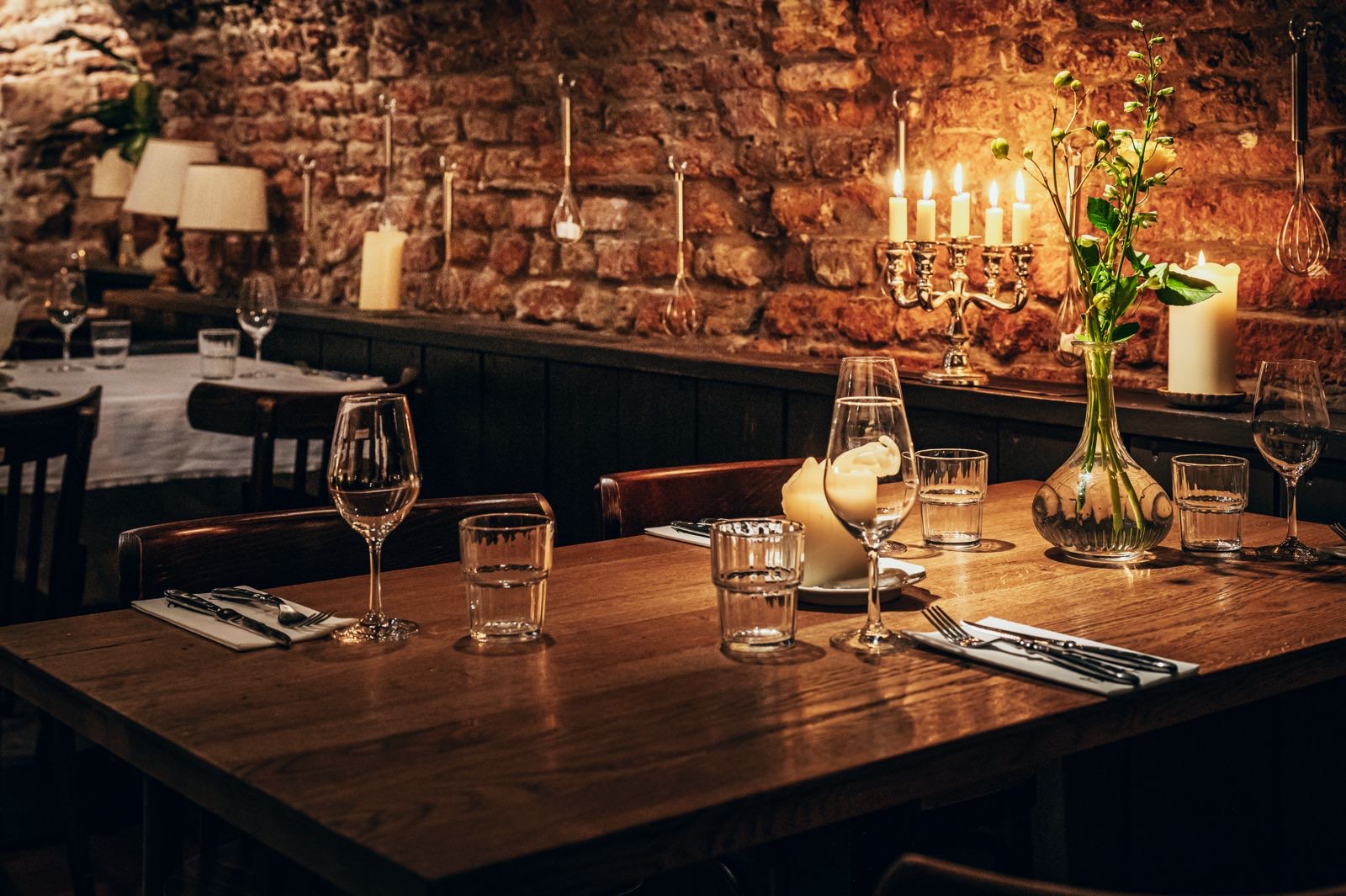 Gedekte tafels in de werfkelder van Bistro aan de Werf, met kaarslicht tegen de bakstenen muur